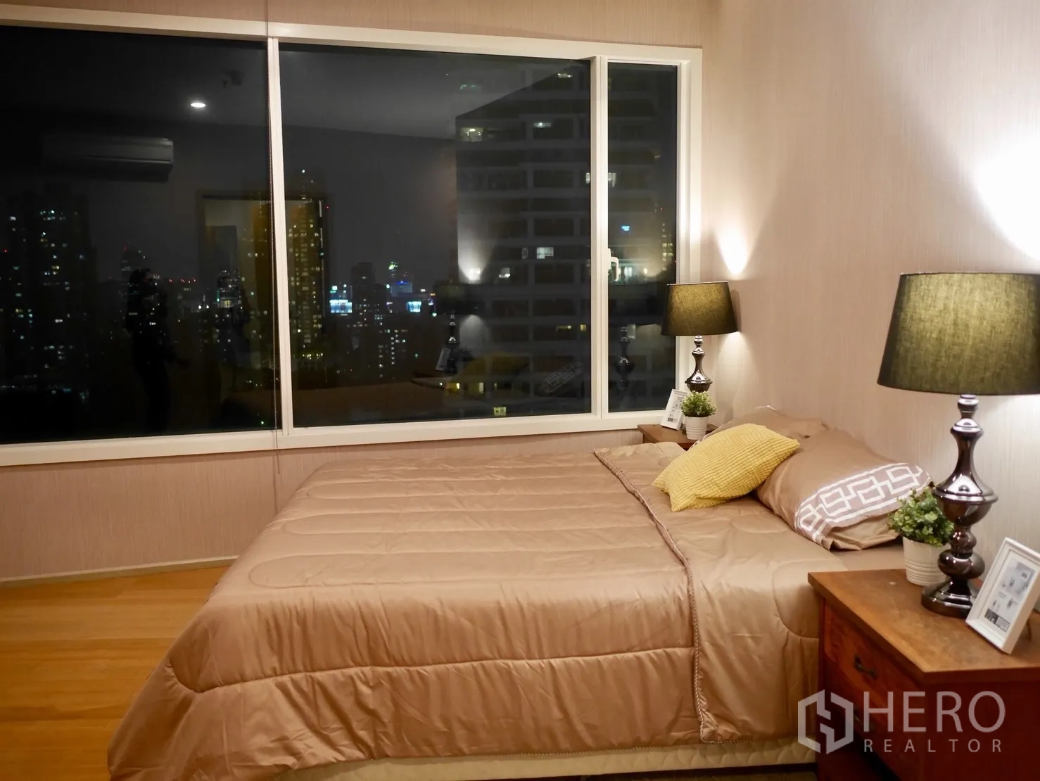 คอนโด ให้เช่าในWatthana, Bangkok - ห้องนอนใหญ่ หน้าต่างบานกว้าง วิวเมืองตอนกลางคืน พร้อมโคมไฟข้างเตียงและพื้นไม้