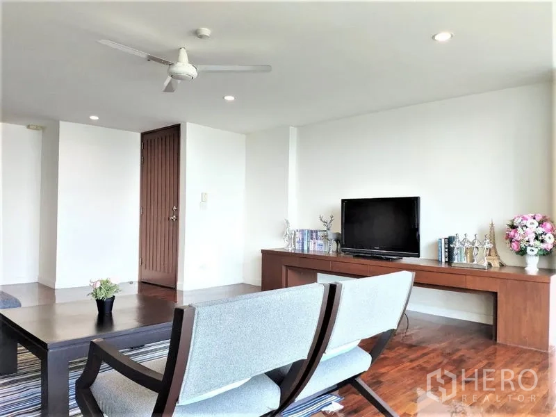 Condominium for rent in Bang Rak, Bangkok - Living room with TV on a long console, lounge chairs, coffee table and ceiling fan over wood floors.