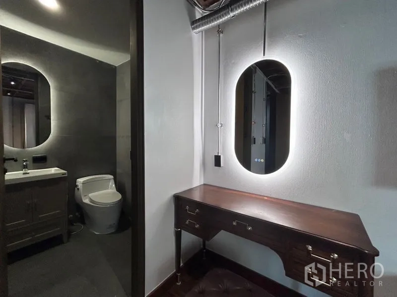 Apartment for rent in Khlong Toei, Bangkok - Dressing nook leading to a gray-tiled bathroom with vanity and toilet, plus visible ceiling ductwork.