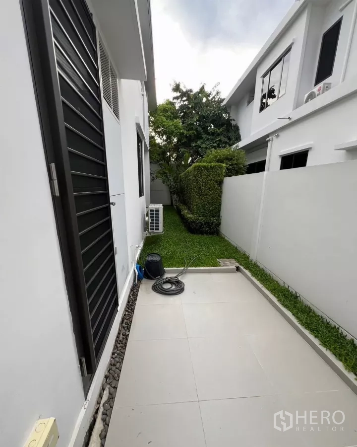 Detached House for rent in Samut Prakan - Service yard with tiled patio, air-conditioning units, and a narrow green strip.