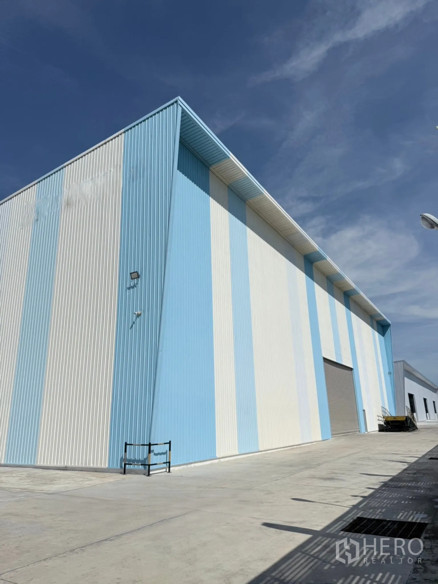 Factory for sale in Ban Bueng, Chon Buri - Striped warehouse facade with big roller door beside a broad loading area.