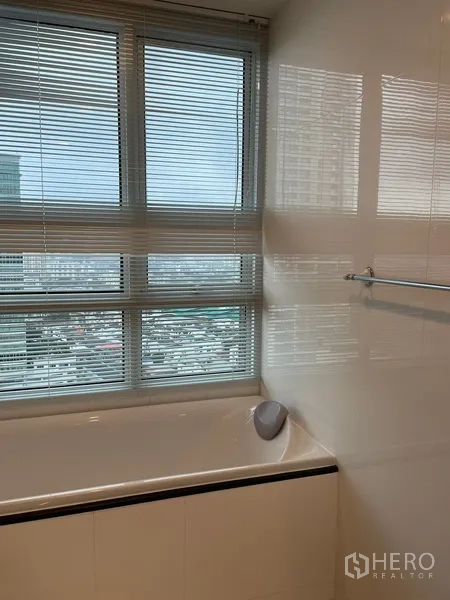 Condominium for rent or sale in Watthana, Bangkok - Bathroom featuring a bathtub beneath a wide window with blinds and open city views.