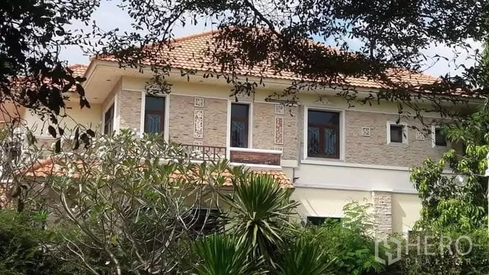 Detached House for sale in Bueng Kum, Bangkok - Upper facade with stone cladding and balcony framed by mature trees.
