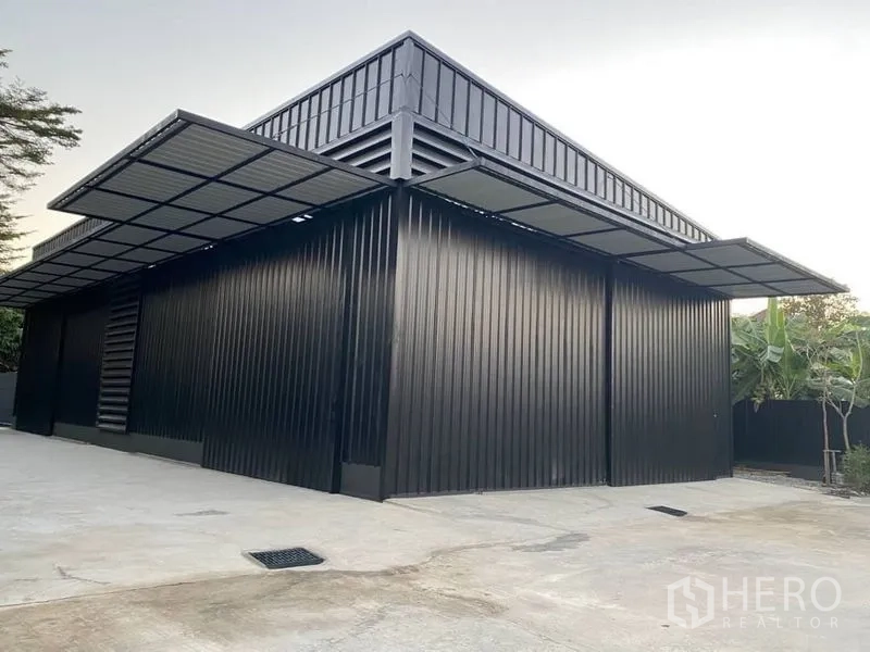 Warehouse for rent in Wang Thonglang, Bangkok - Modern black metal-clad warehouse exterior with wide covered loading bays and large concrete yard.
