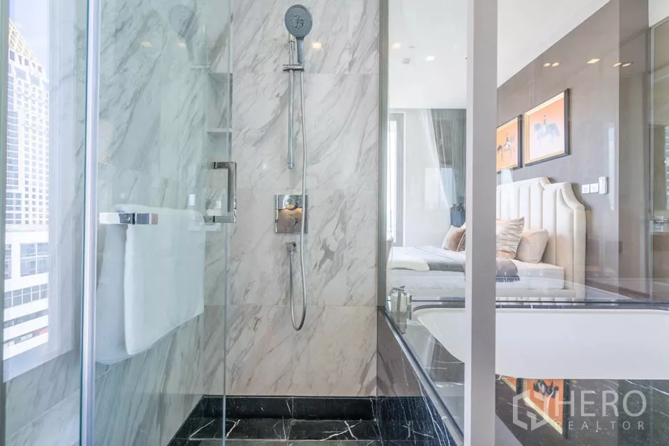 公寓 出租或出售在Bang Rak, Bangkok - 大理石淋浴间，通过玻璃隔断可见卧室景象。