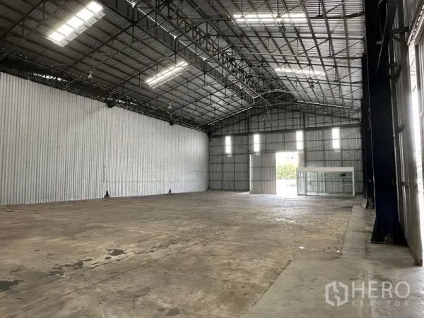 Warehouse for rent in Pak Kret, Nonthaburi - Open storage bay with clerestory windows, wide doorway, and glass office room.