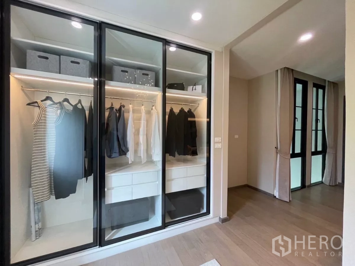 Detached House for rent in Lat Phrao, Bangkok - Walk-in closet with glass sliding doors and built-in hanging rails and drawers.
