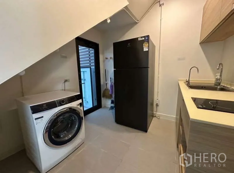 联排别墅 出租在Lat Phrao, Bangkok - 家政厨房区，带水槽、电磁炉、冰箱和洗衣机。