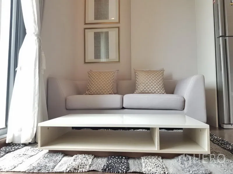 公寓 出租在Ratchathewi, Bangkok - 灰色沙发与靠垫，低矮白色茶几，墙面装饰画点缀。