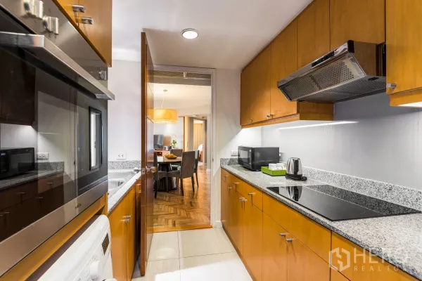 Condominium for rent in Yan Nawa, Bangkok - Kitchen corridor view toward the dining area with electric cooktop, built-in oven, microwave and washing machine.