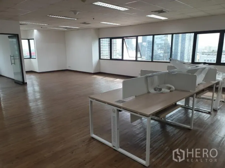 Office Space for rent in Khlong Toei, Bangkok - Open-plan office with wood floors, ceiling lights, a glass-ready meeting area and bench desks by city-facing windows.