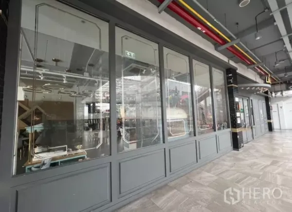 零售空间 出租在Khlong Toei, Bangkok - 社区商场走廊与整排玻璃店面，金属装饰框线。