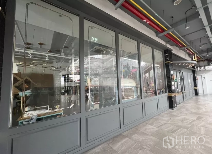 零售空间 出租在Khlong Toei, Bangkok - 社区商场走廊与整排玻璃店面，金属装饰框线。