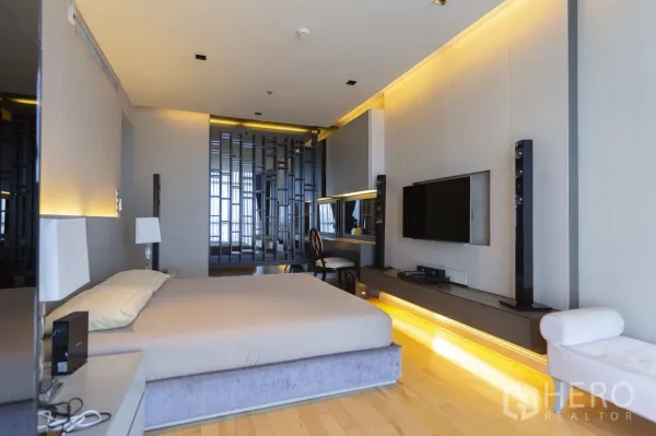 Condominium for rent in Pathum Wan, Bangkok - Modern master bedroom with wood flooring, accent lighting, wall-mounted TV and work desk.