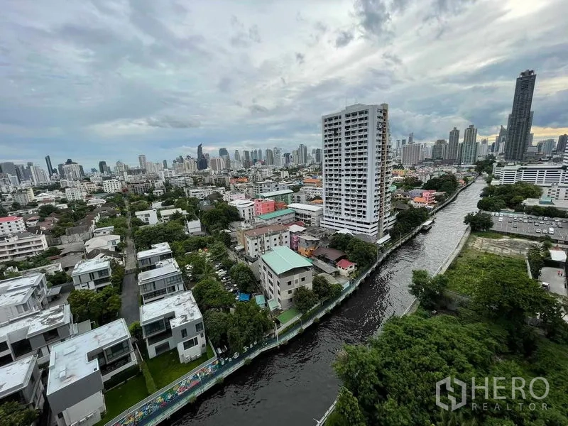 Condominium for sale in Huai Khwang, Bangkok - High-floor balcony outlook over a canal, green neighborhoods and the Bangkok skyline.