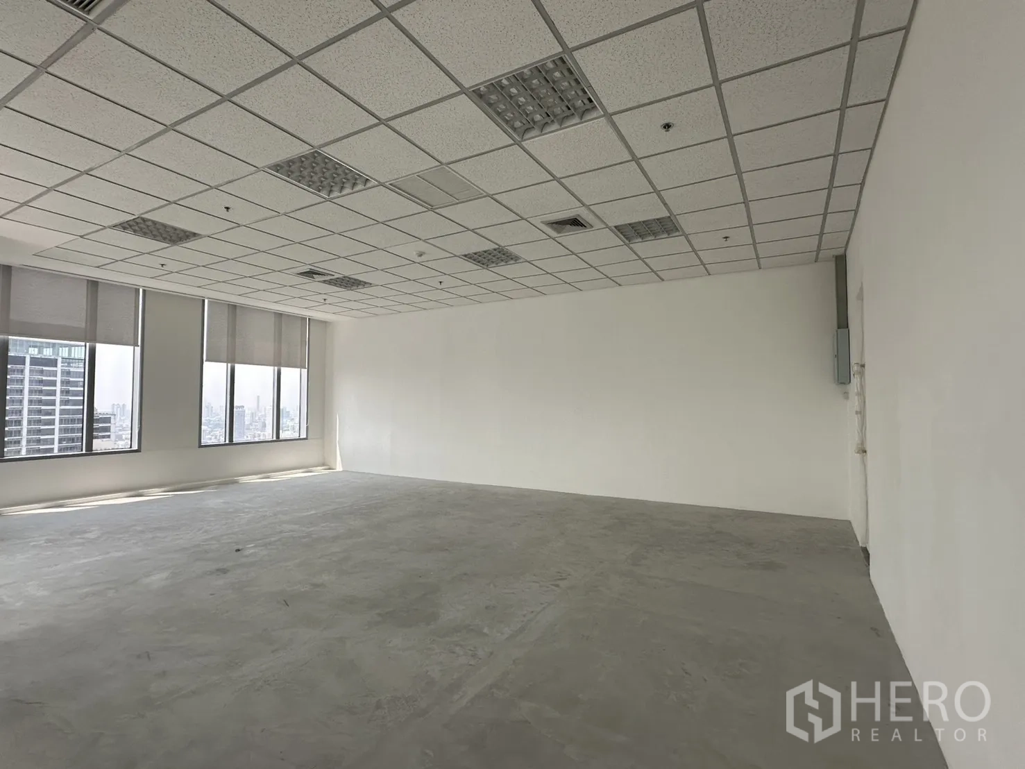 ออฟฟิศ for rent in Khlong Toei, Bangkok - พื้นที่ออฟฟิศโล่ง ผนังสีขาว เพดานแขวนพร้อมไฟ และหน้าต่างบานใหญ่พร้อมมู่ลี่เห็นวิวเมือง