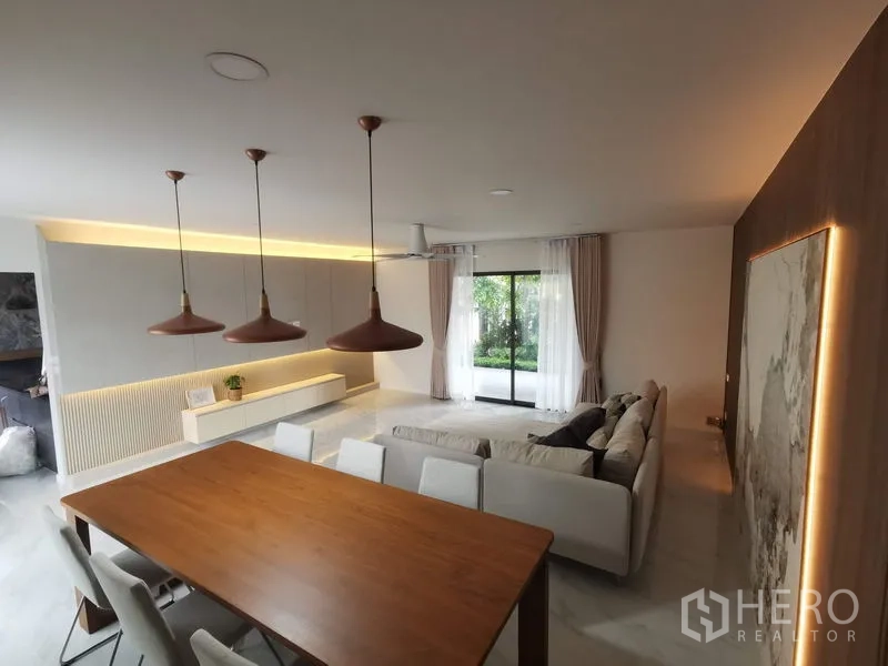 Townhouse for rent in Bang Phli, Samut Prakan - Open-plan dining and living room with wood table, trio of pendant lights and glass doors to garden.