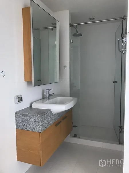 Condominium for rent in Bang Rak, Bangkok - Contemporary bathroom with floating vanity, large mirror and glass-enclosed rainfall shower.