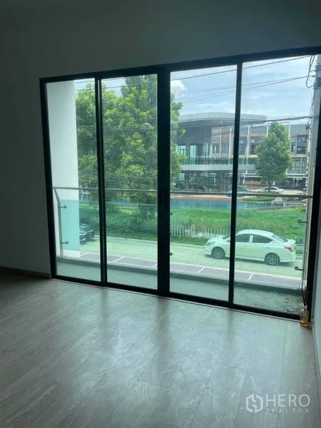 Townhouse for sale in Bueng Kum, Bangkok - Upper-floor room with full-height sliding doors opening to a street-facing balcony.
