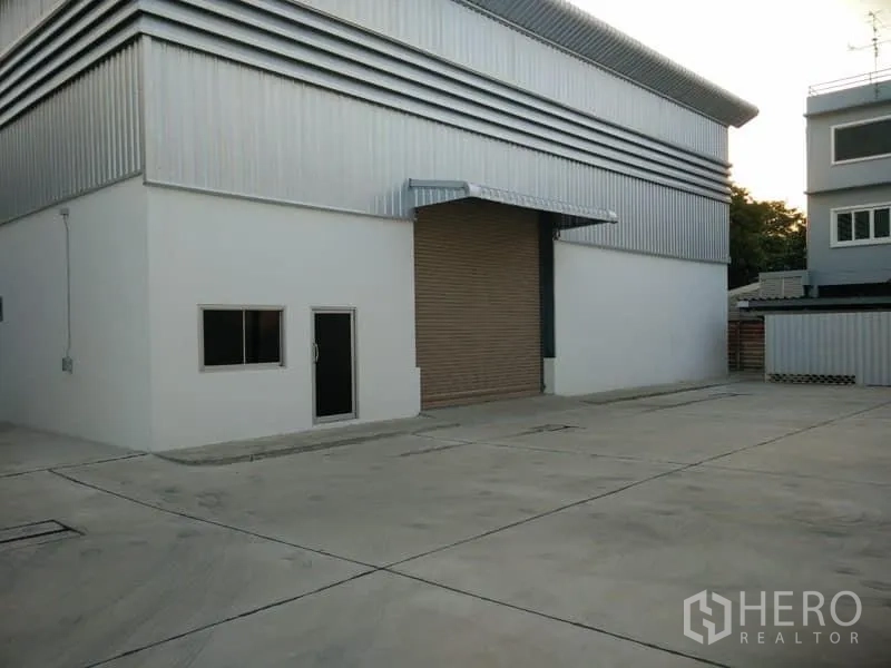 Warehouse for rent in Suan Luang, Bangkok - Warehouse exterior with roller-shutter loading bay, side door and windows on a large paved yard.