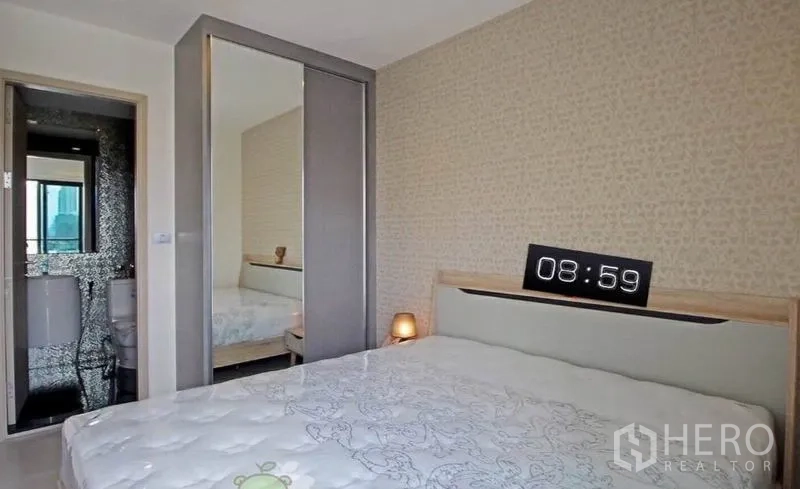 Condominium for rent in Khlong Toei, Bangkok - Bedroom with mirrored wardrobe and doorway to the en-suite bathroom.