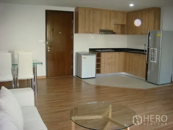 Apartment for rent in Khlong Toei, Bangkok - Open-plan living area with wood-tone L-shaped kitchen, refrigerator and dining set in an Asok apartment.