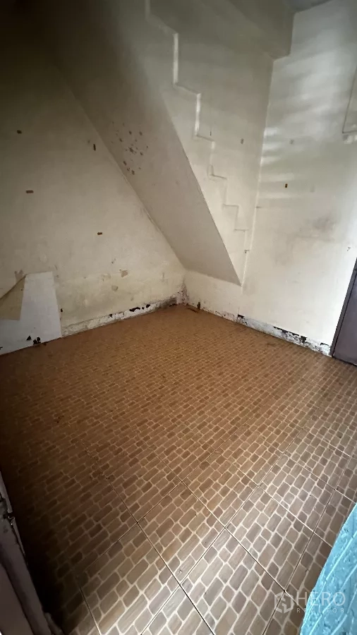 Shophouse for rent in Chatuchak, Bangkok - Under-stair area with tiled flooring and plain walls showing wear, ideal for storage or utility space.