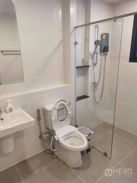 Detached House for rent in Bang Phli, Samut Prakan - Clean bathroom with glass-enclosed shower, toilet and wall-mounted sink in white tiles.