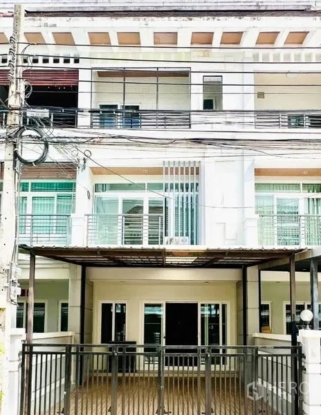 联排别墅 出租在Prawet, Bangkok - 三层联排别墅外立面，带阳台、栅栏车位与大窗，位于Srinakarin社区