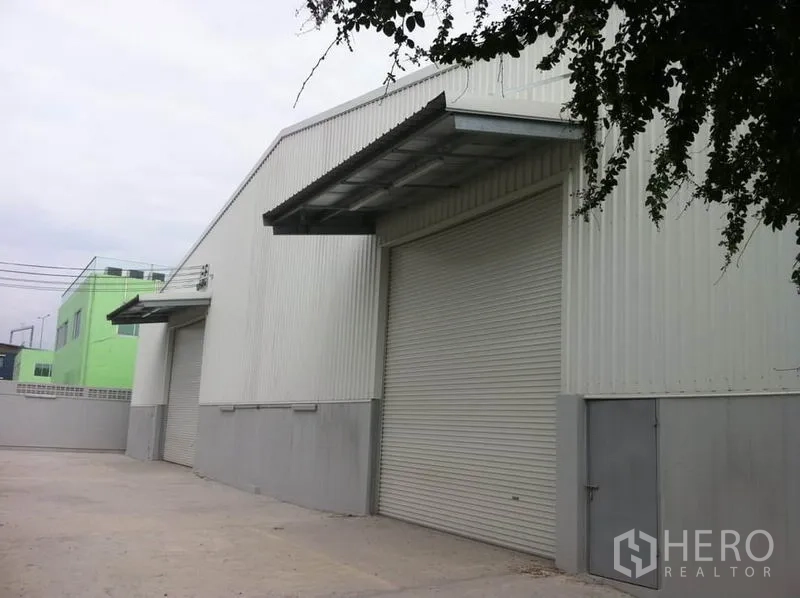 คลังสินค้า ให้เช่าในSai Mai, Bangkok - ด้านนอกโกดังเมทัลชีท มีประตูม้วนหลายจุด กันสาดลานขนถ่าย และลานคอนกรีตกว้างสำหรับรถบรรทุก