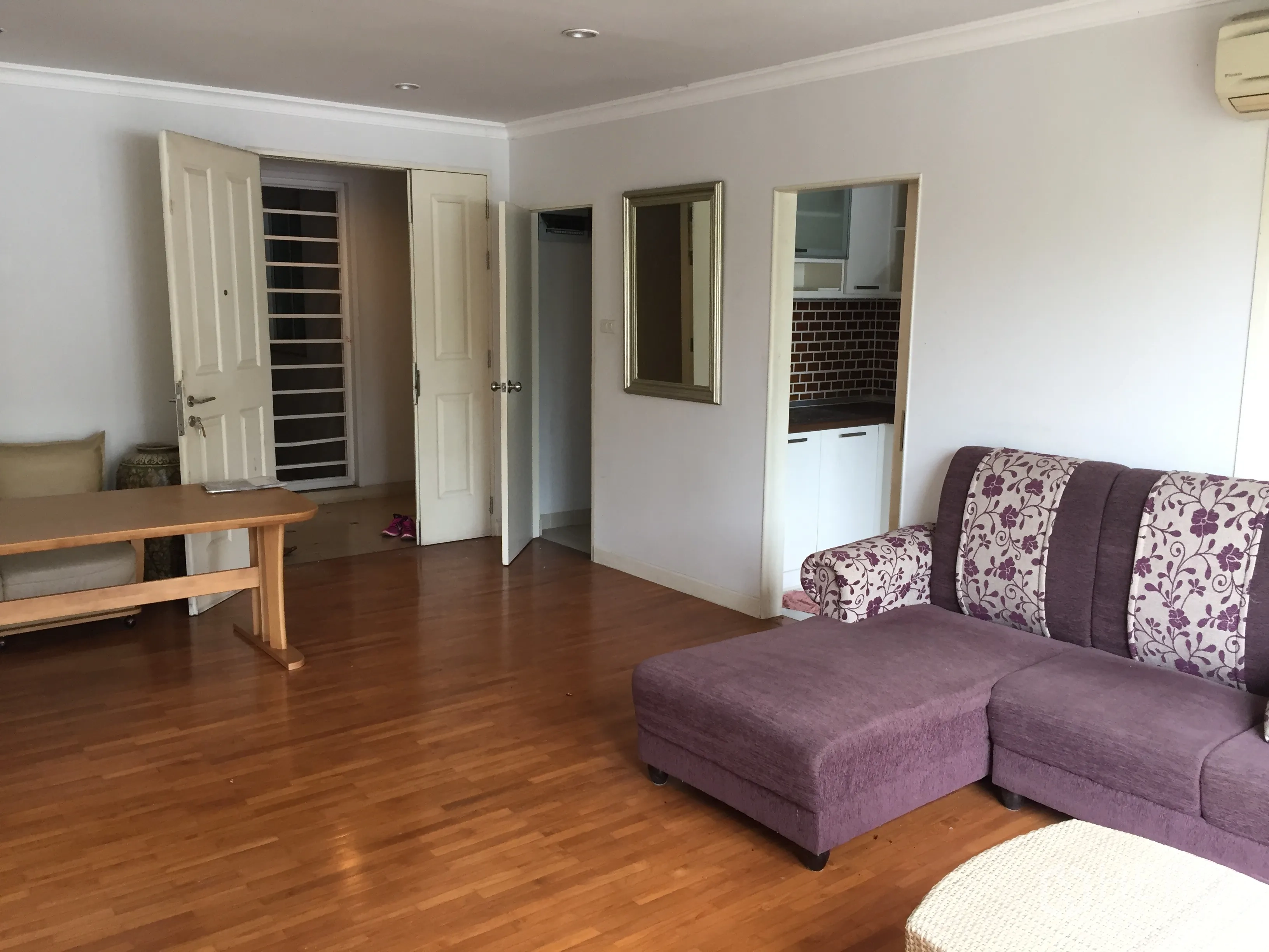 Condominium for sale in Khlong Toei, Bangkok - Bright living room with wood flooring, purple sectional sofa and doorway to separate kitchen.