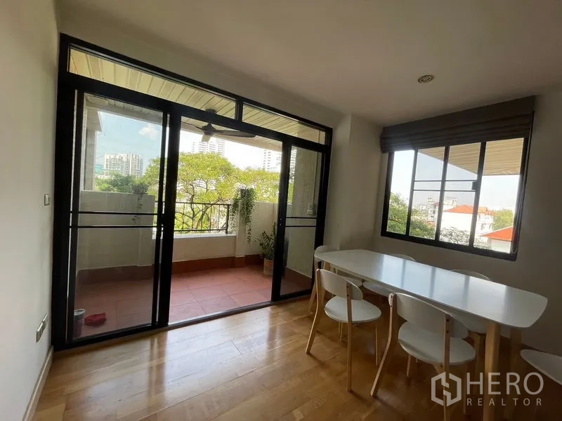 Condominium for rent in Watthana, Bangkok - Dining area with large windows and glass doors opening to a leafy terrace.