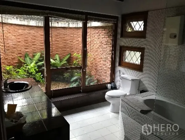 Detached House for rent in Khlong Toei, Bangkok - Bathroom with bathtub, garden-facing glass doors, and a red brick privacy wall.