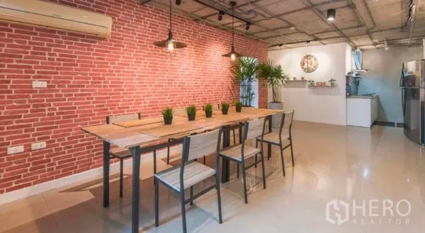 Condominium for rent in Watthana, Bangkok - Open-plan dining area with long wooden table, pendant lights and red brick feature wall.