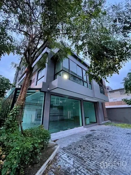 Detached House for rent or sale in Khlong Toei, Bangkok - Modern three-storey detached house with large corner windows, glass walls and a driveway under mature trees in Khlong Toei.