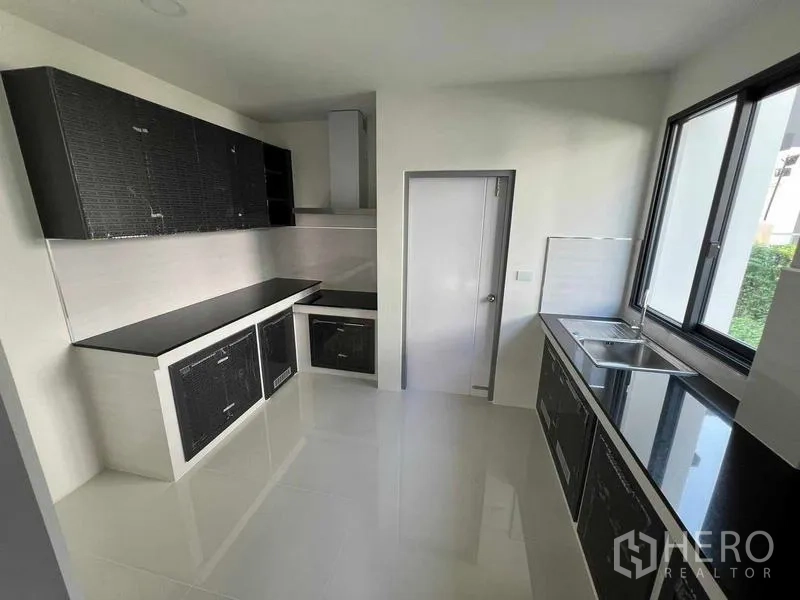 Detached House for rent in Khlong Sam Wa, Bangkok - Closed kitchen with black cabinetry, stone countertops, range hood and a large window.