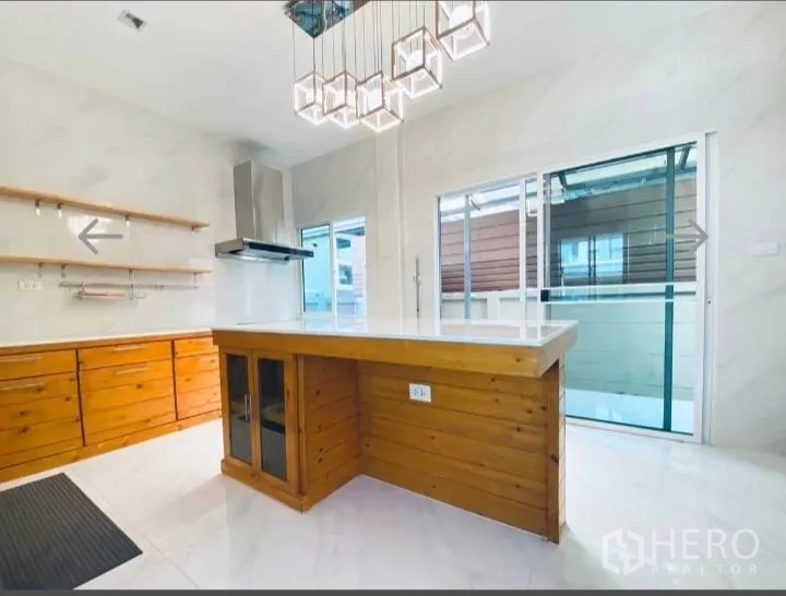 Detached House for sale in Saphan Sung, Bangkok - Bright kitchen with wooden island, pendant lights and sliding doors to the patio.