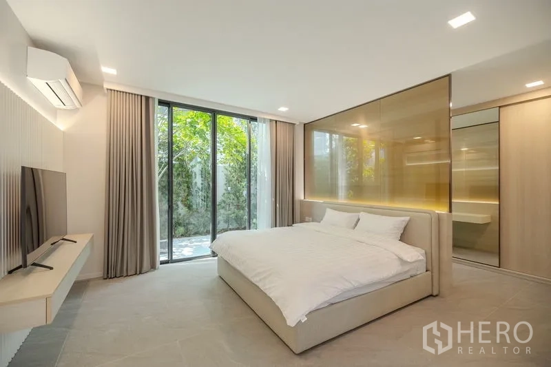 Detached House for rent in Saphan Sung, Bangkok - Garden-level bedroom with sliding doors, TV wall and golden glass partition.