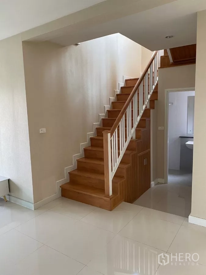 บ้าน ให้เช่าหรือขายในSuan Luang, Bangkok - บันไดไม้ราวสีขาว มีตู้เก็บของใต้บันได ข้างห้องน้ำชั้นล่าง