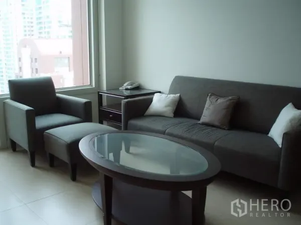 คอนโด ให้เช่าในRatchathewi, Bangkok - ห้องนั่งเล่นสว่างพร้อมโซฟาสีเทา เก้าอี้พักผ่อน โต๊ะกลางกระจก และหน้าต่างบานใหญ่เห็นวิวเมือง ในคอนโด 1 ห้องนอนย่านราชเทวี กรุงเทพฯ