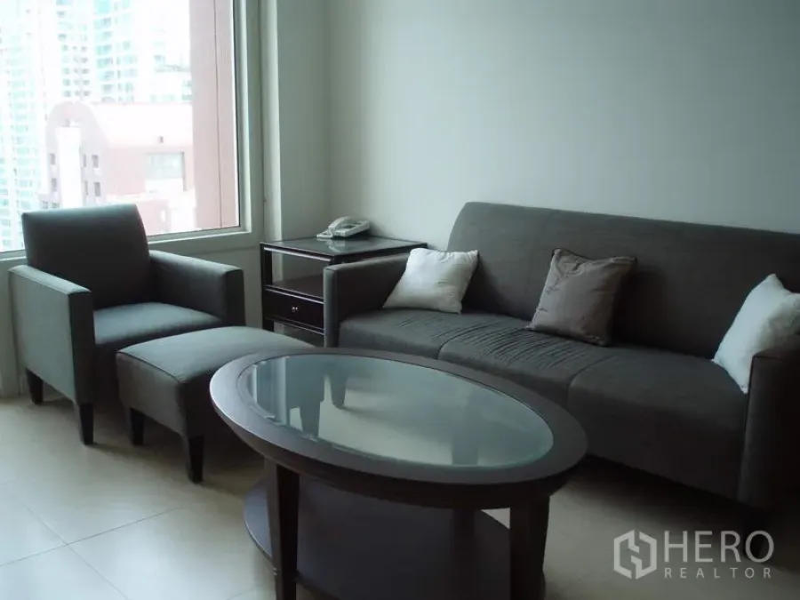 คอนโด ให้เช่าในRatchathewi, Bangkok - ห้องนั่งเล่นสว่างพร้อมโซฟาสีเทา เก้าอี้พักผ่อน โต๊ะกลางกระจก และหน้าต่างบานใหญ่เห็นวิวเมือง ในคอนโด 1 ห้องนอนย่านราชเทวี กรุงเทพฯ