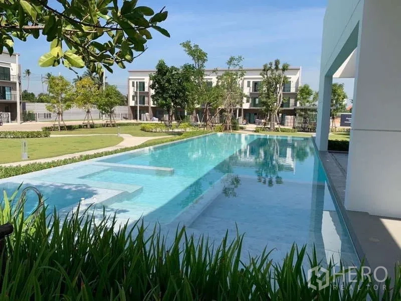 Townhouse for rent or sale in Phasi Charoen, Bangkok - Outdoor swimming pool beside green lawn and trees in the common area.
