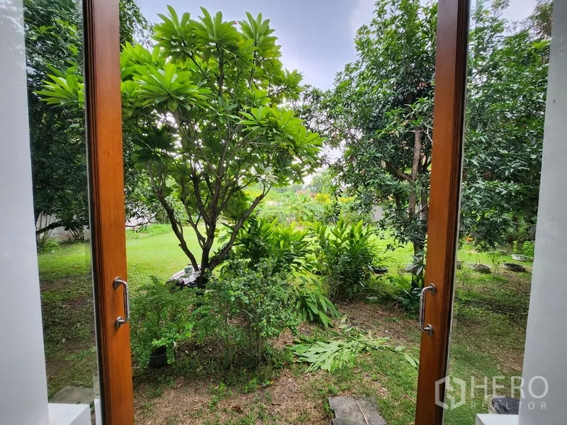 独立式住宅 出租在Prawet, Bangkok - 木质法式门框出的花园景，热带乔木与草坪郁郁葱葱。