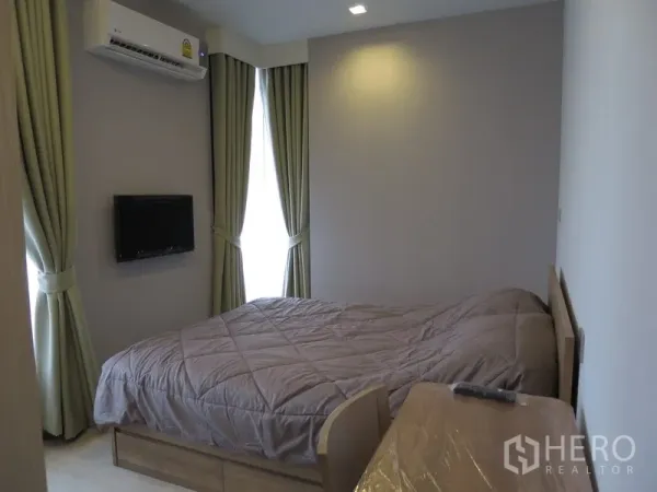 Condominium for rent in Watthana, Bangkok - Bedroom with a double bed, wall-mounted TV, air conditioner, and floor-to-ceiling curtained windows.