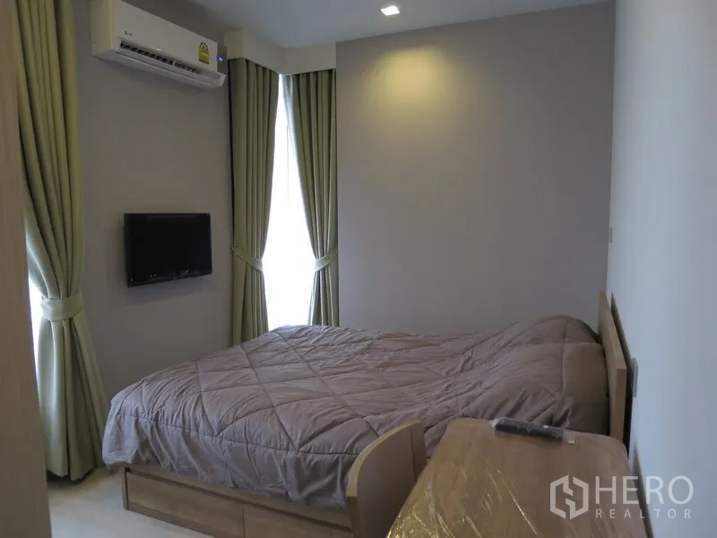 Condominium for rent in Watthana, Bangkok - Bedroom with a double bed, wall-mounted TV, air conditioner, and floor-to-ceiling curtained windows.