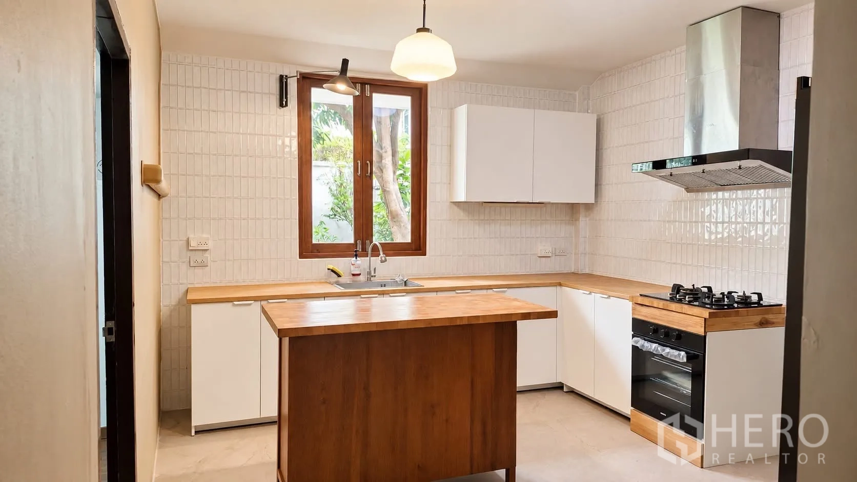 Detached House for rent in Khlong Toei, Bangkok - Kitchen view showing gas hob, oven, tiled backsplash, and island.