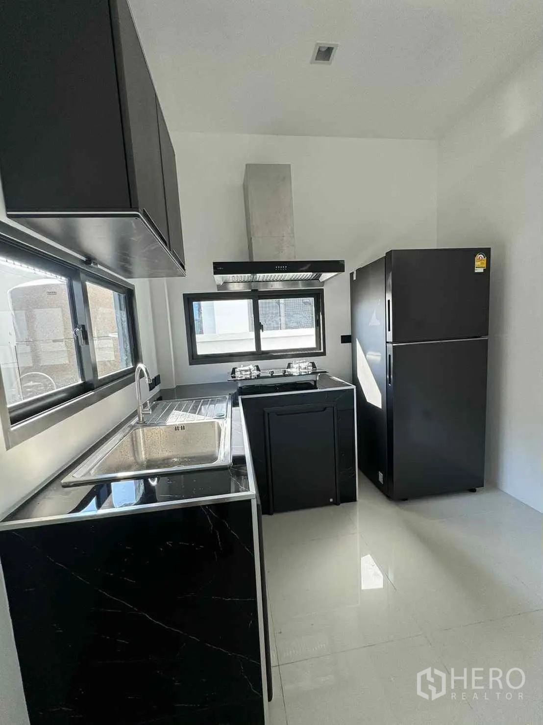 Detached House for rent in Bang Phli, Samut Prakan - Modern separate kitchen with black cabinets, gas hob, hood, sink and refrigerator.