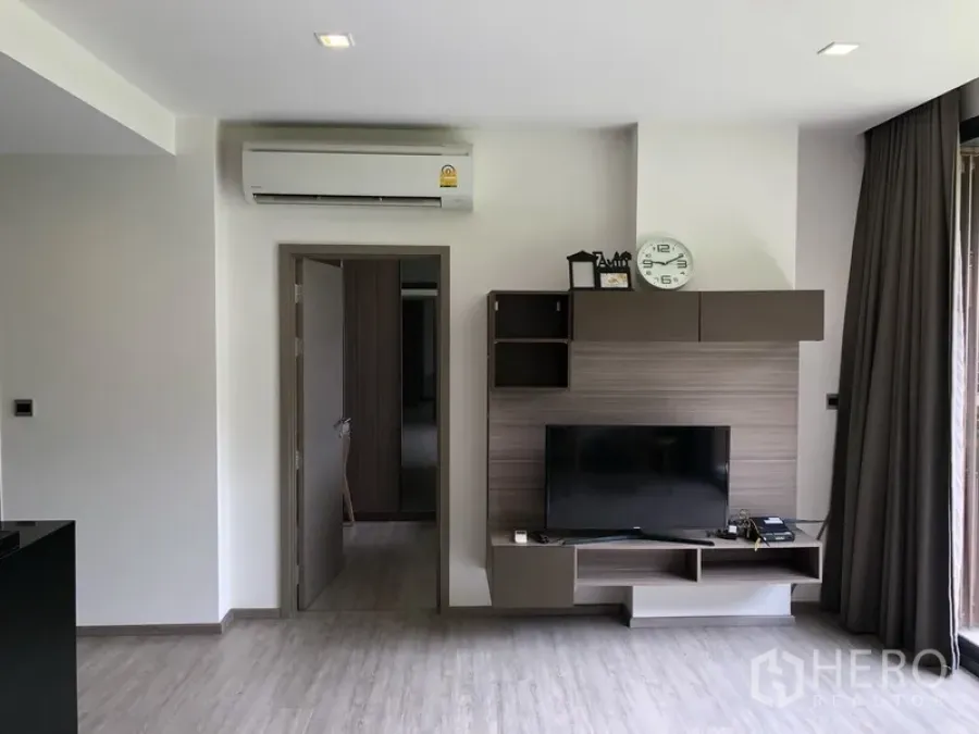 Condominium for rent in Watthana, Bangkok - Modern living room at Mori Haus with built-in TV wall, air conditioner, and sliding glass door to the balcony.