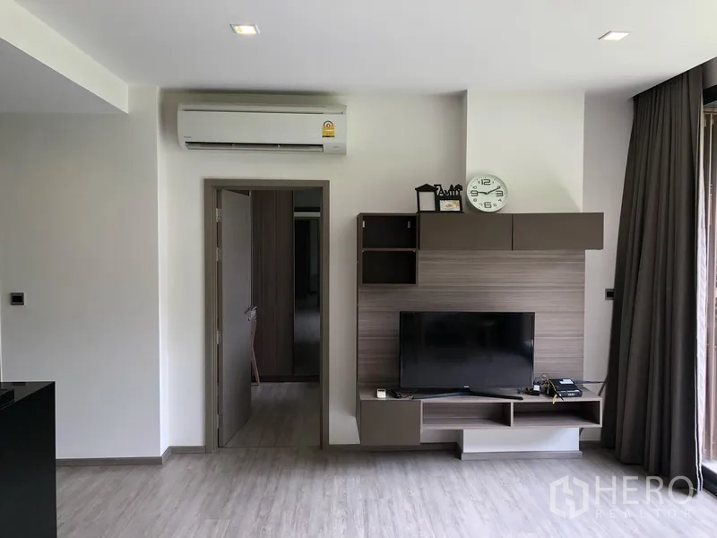 Condominium for rent in Watthana, Bangkok - Modern living room at Mori Haus with built-in TV wall, air conditioner, and sliding glass door to the balcony.