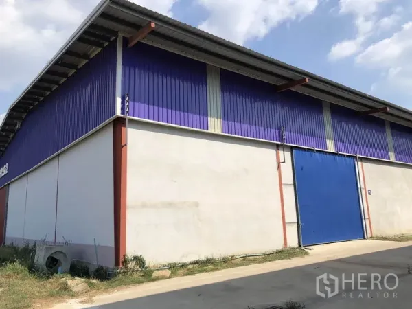 Warehouse for rent in Sai Noi, Nonthaburi - Corner view of the warehouse showing the high roof, purple cladding, blue door and truck-friendly access lane.